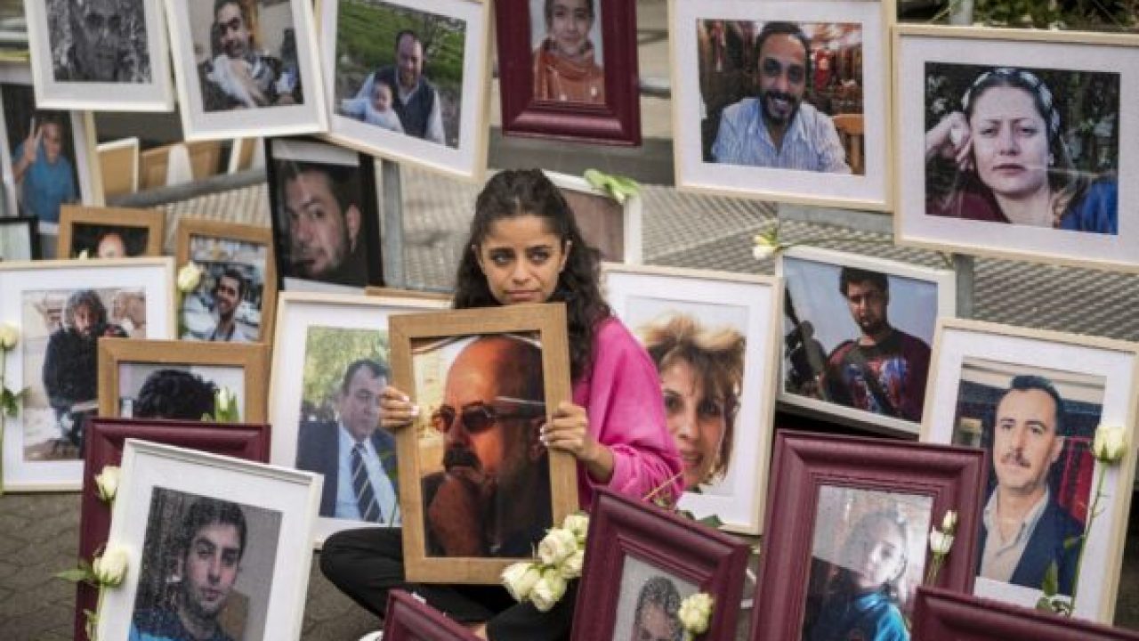 (FILES) In this file photo taken on June 04, 2020 Syrian campaigner Wafa Mustafa sits between pictures of victims of the Syrian regime as she holds a picture of her father, during a protest outside the trial against two Syrian alleged former intelligence officers accused for crimes against humanity, in the first trial of its kind to emerge from the Syrian conflict, in Koblenz, western Germany. - As Germany prepares to issue the verdict on January 13, 2022 in the first trial worldwide over state-sponsored torture in Syria, Wafa Mustafa is one of many Syrians still looking for relatives missing since a brutal government crackdown on dissent began in 2011. The trial of Anwar Raslan, a former colonel in Bashar al-Assad's regime, is an important "first step", Mustafa tells AFP. (Photo by Thomas Lohnes / AFP)