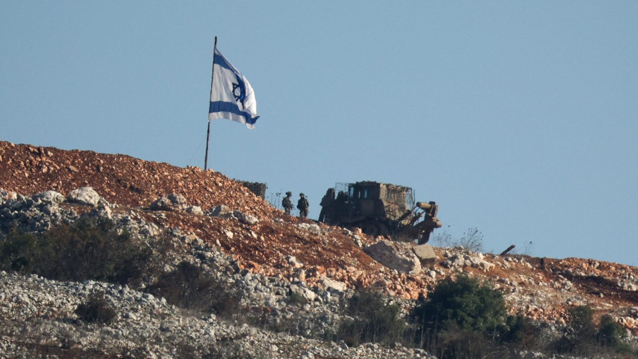 Israeli soldiers stand under an Israeli flag in southern Lebanon, near the Israel-Lebanon border, after the ceasefire between Israel and Hezbollah took effect, as seen from northern Israel, November 30, 2024. REUTERS/Stoyan Nenov