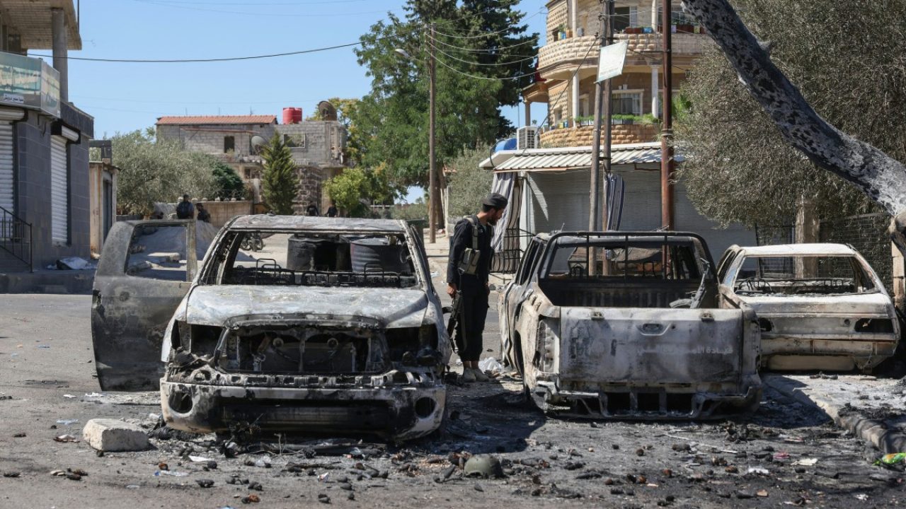 A member of Syrian security forces looks at burnt vehicles amid ongoing clashes in the southern city of Sweida on July 16, 2025. Damascus deployed troops in the predominantly Druze province of Sweida, after clashes between Druze fighters and Bedouin tribes killed scores of people, with Syria's defence minister declaring a ceasefire on July 15 in Sweida city, which government forces entered in the morning. (Photo by Bakr ALkasem / AFP)