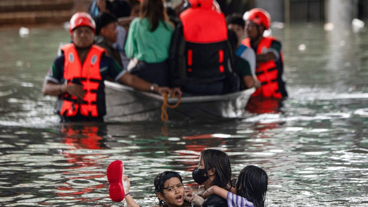 People swim through the floodwater on a street in Manila on July 21, 2025, after Typhoon Wipha brought heavy rains and flooding to the Philippines, where two people have been reported missing, according to the country's National Disaster Risk Reduction and Management Council.  (Photo by Ted ALJIBE / AFP)