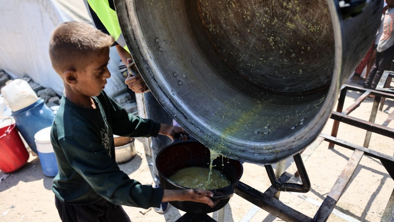 A Palestinian boy receives the last drops of lentil soup at a food distribution point in Gaza City on August 1, 2025. (Photo by Omar AL-QATTAA / AFP)