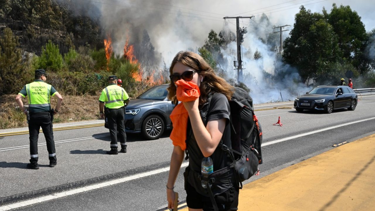 A pilgrim on her way to Santiago de Compostela covers her mouth as she walks past a wildfire near the village of Mougas, in Oia municipality, northwestern Spain on August 22, 2025. The northwestern regions of Galicia and Castile and Leon, along with Extremadura in the west, have been hit hardest by the fires raging since early August in the scorching heat. More than 403,000 hectares (996,000 acres) have been burnt in Spain this year, according to the European Forest Fire Information System. (Photo by MIGUEL RIOPA / AFP)