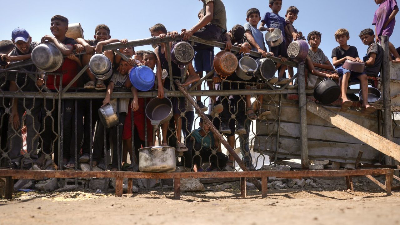 Children gather by a fence as they try to get rice from a charity kitchen providing food for free in the west of Gaza City, on August 28, 2025, as the war between Israel and the Hamas militants movement continues. The UN declared a famine in Gaza governorate last week, blaming "systematic obstruction" of humanitarian deliveries by Israel. (Photo by BASHAR TALEB / AFP)