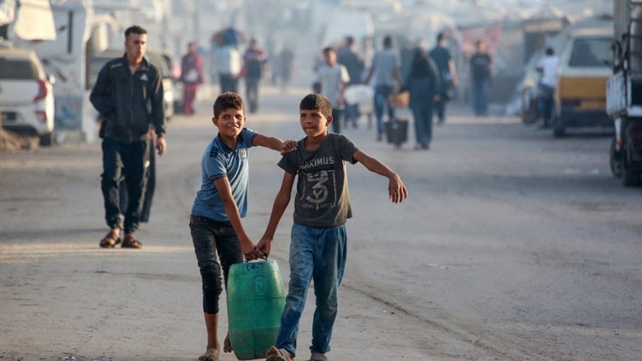 Displaced Palestinian boys carry a gallon of water in Deir el-Balah in the central Gaza Strip, on October 5, 2025. Negotiators were converging on Cairo on October 5 ahead of talks aimed at ending nearly two years of war in Gaza, with Israel's leader expressing hope that the hostages still being held there would be released in a matter of days. (Photo by Bashar TALEB / AFP)