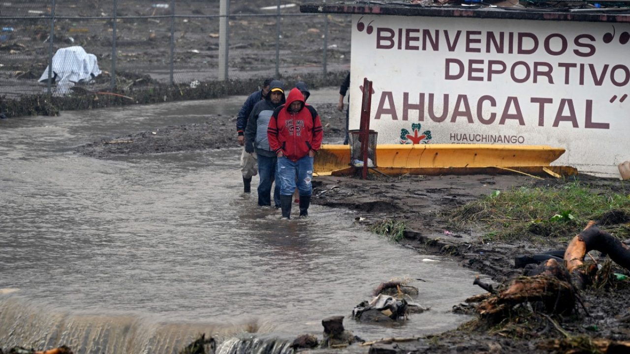 People wade through a flooded street due to the rains in the municipality of Huauchinango, Puebla State, Mexico on October 11, 2025. The death toll from heavy rains in Mexico rose to 37 on Saturday after nine more fatalities were confirmed, the Mexican government reported. (Photo by Alfredo ESTRELLA / AFP)