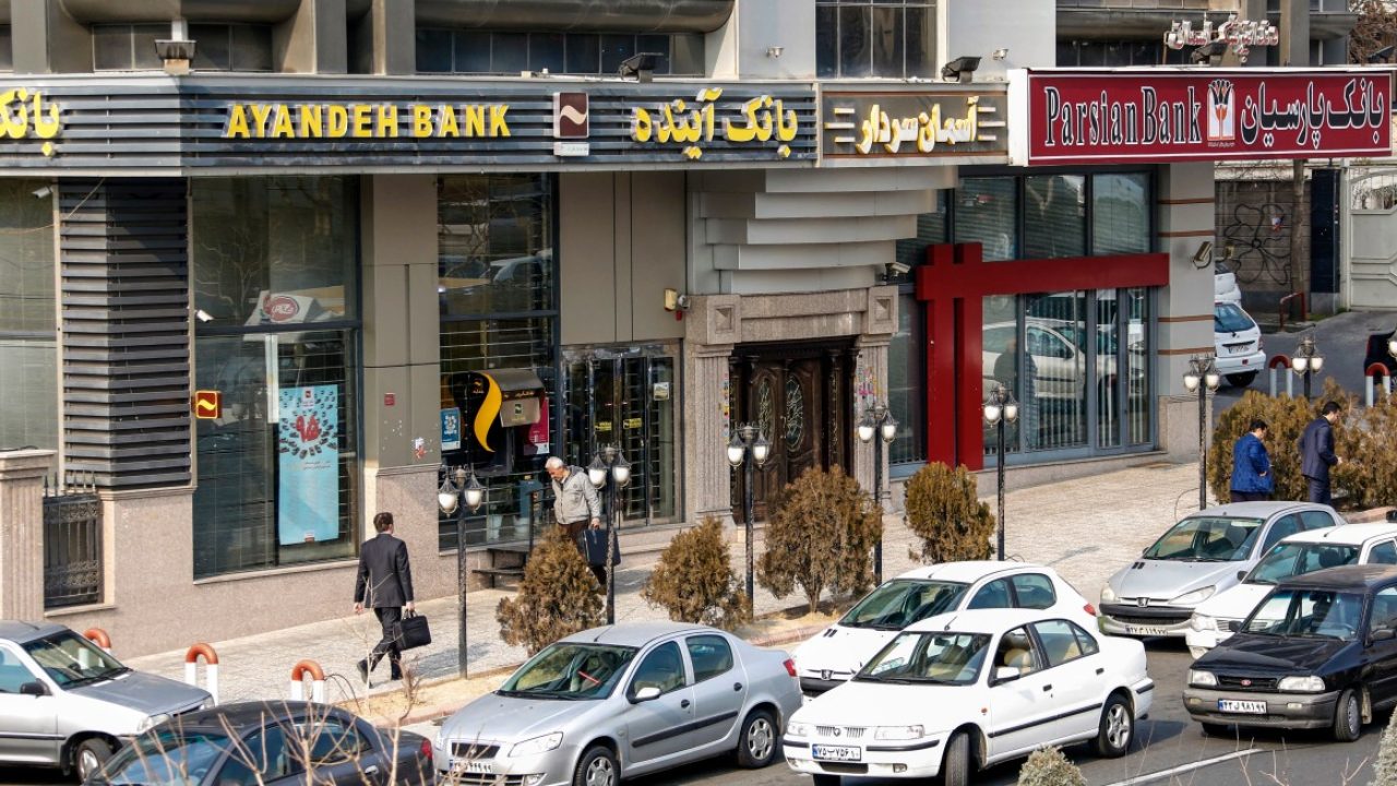 FILES-IRAN-ECONOMY-BANKING (FILES) Iranians walk past an Ayandeh Bank branch (L) in the capital Tehran on January 14, 2017. Iran declared Ayandeh Bank bankrupt with its assets absorbed by the state, official media reported October 25, 2025, in a rare move in the country grappling with international sanctions. Founded in 2012, the private bank had a network of 270 branches across the country, including 150 in the capital Tehran alone. (Photo by ATTA KENARE / AFP)
