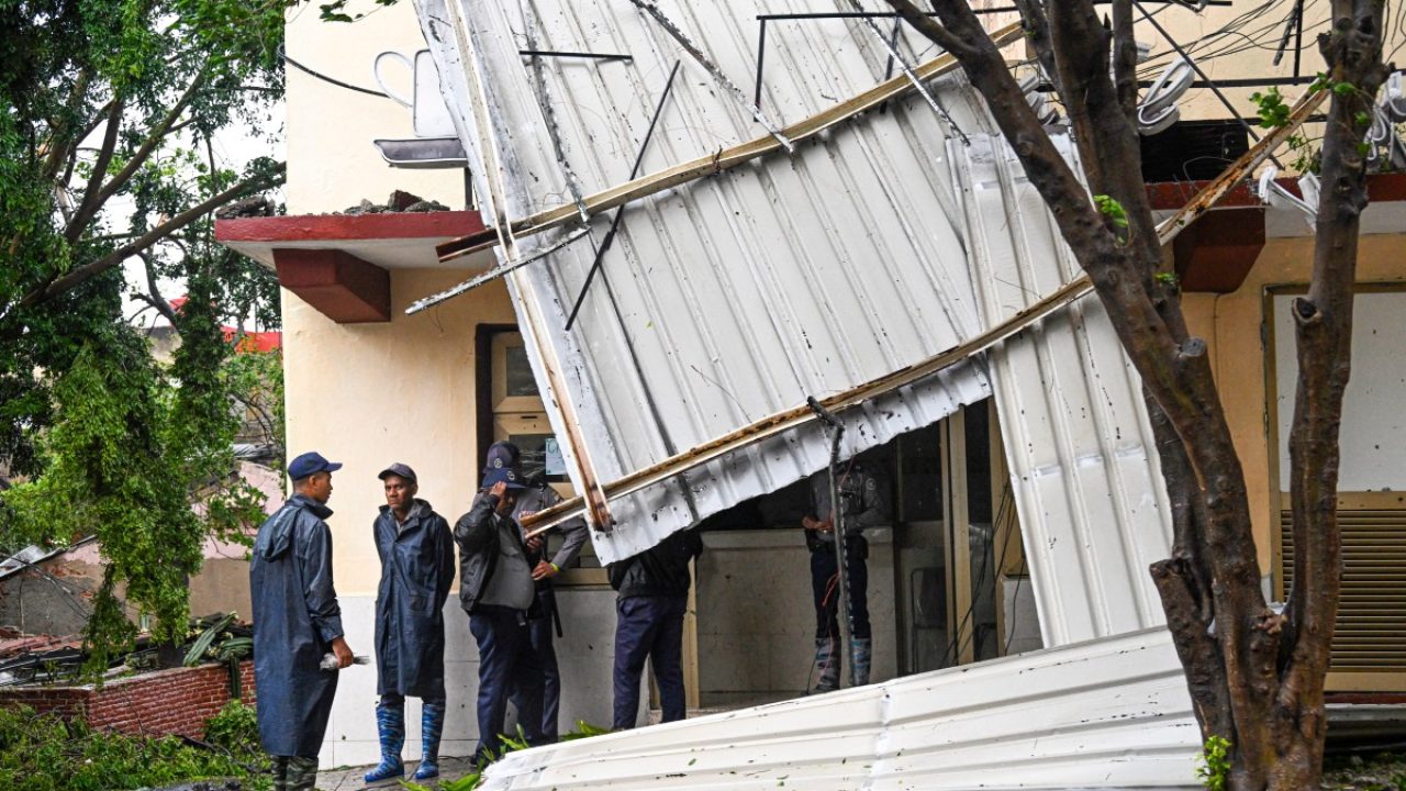 CUBA-WEATHER-HURRICANE-MELISSA Police officers stand guard outside a damaged state-owned building after Hurricane Melissa struck a neighborhood in Santiago de Cuba on October 29, 2025. A powerful Hurricane Melissa made landfall in eastern Cuba on Wednesday, causing damage and flooding to homes and streets in Santiago de Cuba province, an AFP team on the ground reported. (Photo by YAMIL LAGE / AFP)