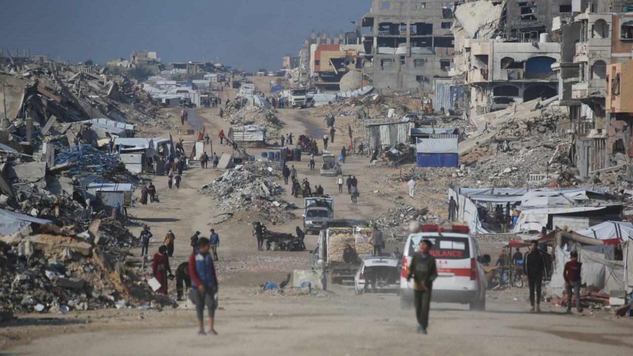 Palestinians walk in a street next to the rubble of destroyed buildings in the Jabalia refugee camp, in the northern Gaza Strip on December 24, 2025. (Photo by Bashar Taleb / AFP)