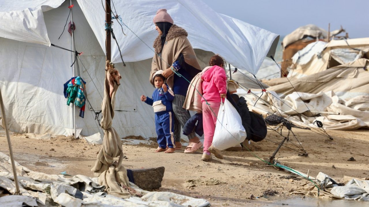 A displaced Palestinian woman holds a child next to tents and makeshift shelters as the region experiences cold winter conditions in Al-Mawasi refuge camp in the southern Gaza Strip on December 29, 2025. Beginning in October, a fragile ceasefire has so far halted two years of war between Israel and Hamas in the Gaza Strip despite both sides trading accusations of truce violations. (Photo by AFP)