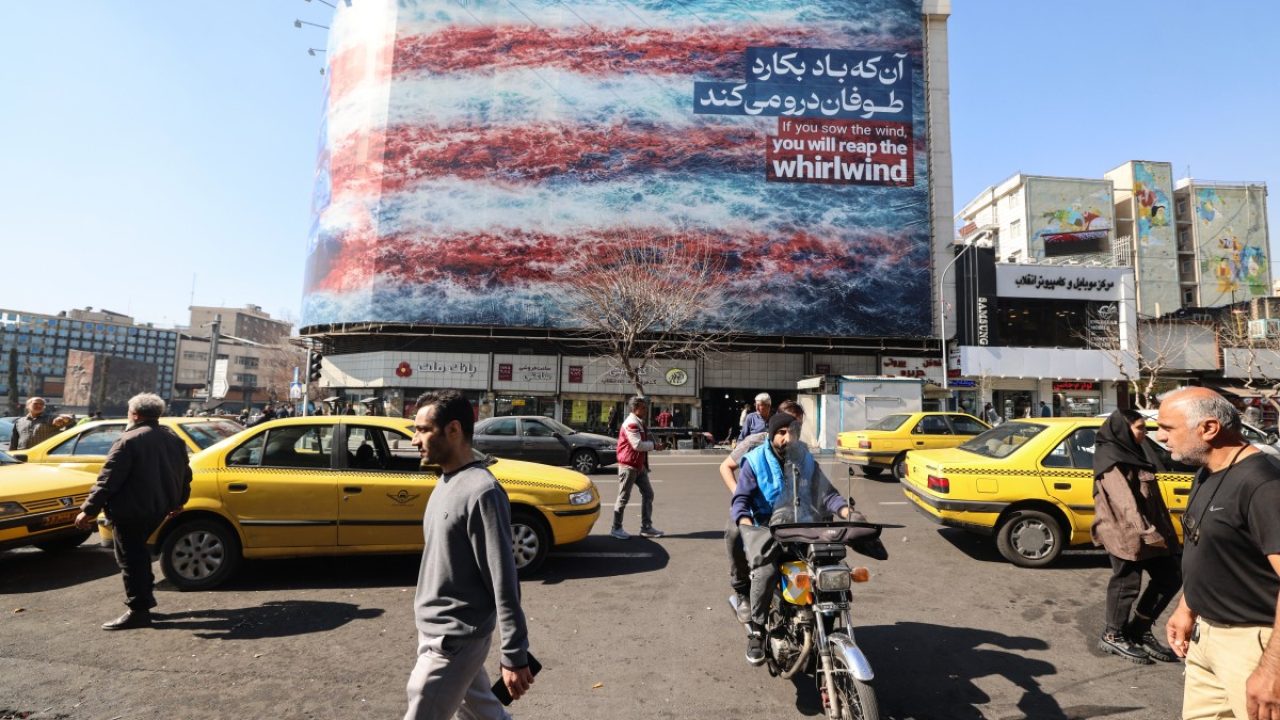 Iranians walk past an anti-US billboard installed on a building on Enqelab Square in Tehran on February 17, 2026. (Photo by ATTA KENARE / AFP)