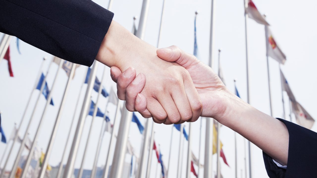 Two business people shaking hands in Beijing, flags flying in the background