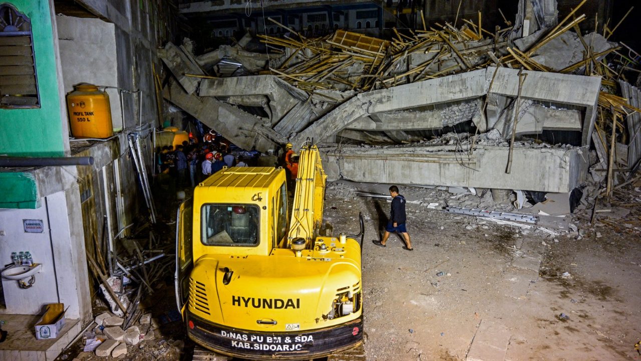 Rescue personnel and locals stand behind an excavator as they search for survivors after a building collapsed at an Islamic boarding school in Sidoarjo, East Java province on September 29, 2025, injuring a number of students and trapping several others under the rubble. (Photo by Juni KRISWANTO / AFP)