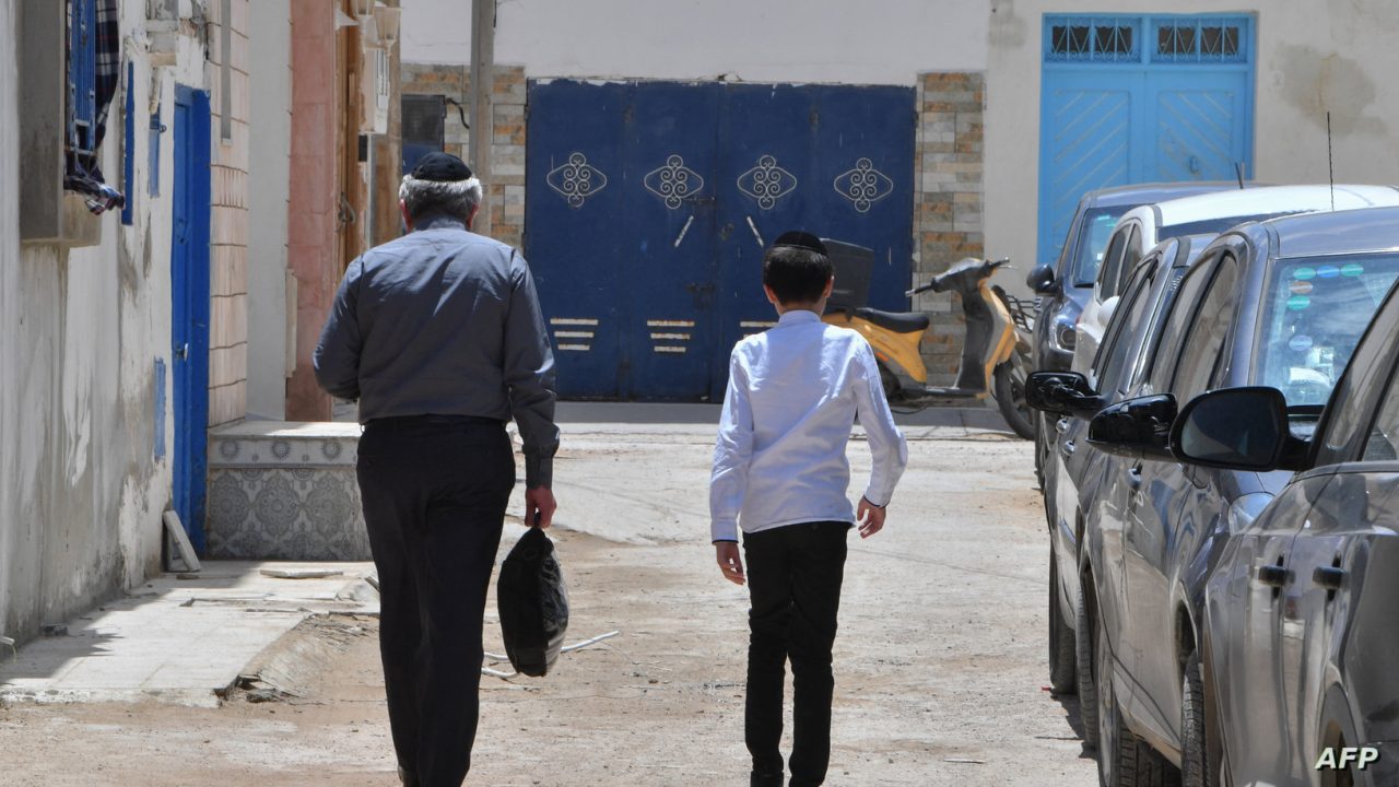 A Jewish man and a child walk through the Hara Kebira, the main Jewish quarter in the resort island of Djerba, near the Ghriba synagogue following a shooting spree by a police officer on the southern Tunisian island on May 10, 2023. Tunisian authorities were investigating the shootings that claimed five lives and sparked mass panic during a Jewish pilgrimage at Africa's oldest synagogue today. (Photo by FETHI BELAID / AFP)