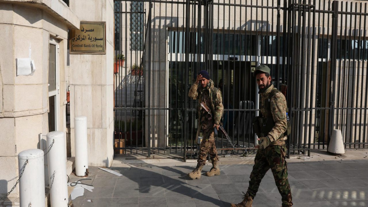 Rebel fighters walk in front of Syrian Central Bank, after rebels seized the capital and ousted President Bashar al-Assad, in Damascus, Syria, December 9, 2024. REUTERS/Mohamed Azakir