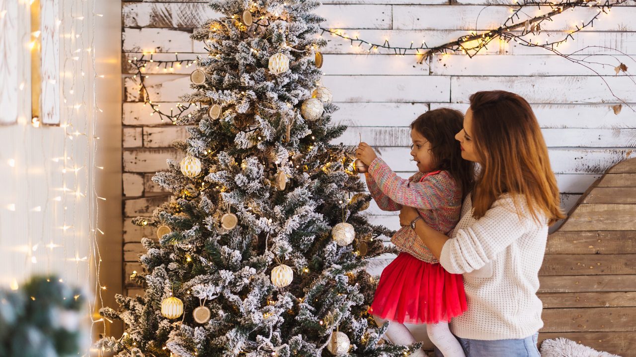 Happy mother and little daughter decorating christmas tree at home