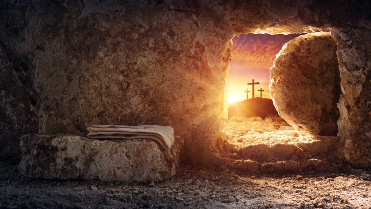 Empty tomb of Jesus at sunrise with crosses in background