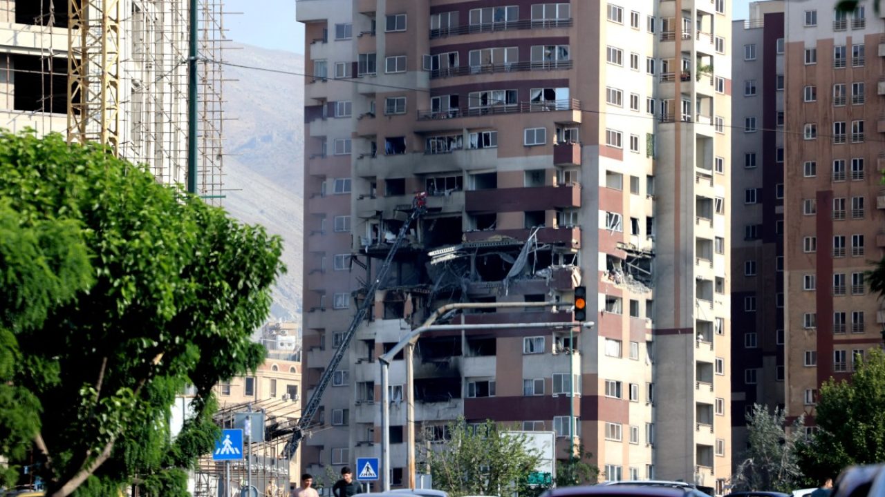 People walk past traffic in front of a building targeted by an Israeli strike in the Iranian capital Tehran on June 13, 2025. Israel carried out strikes against Iran early on June 13, targeting its nuclear and military sites as well as residential buildings in Tehran, after US President Donald Trump warned of a possible "massive conflict" in the region. (Photo by ATTA KENARE / AFP)