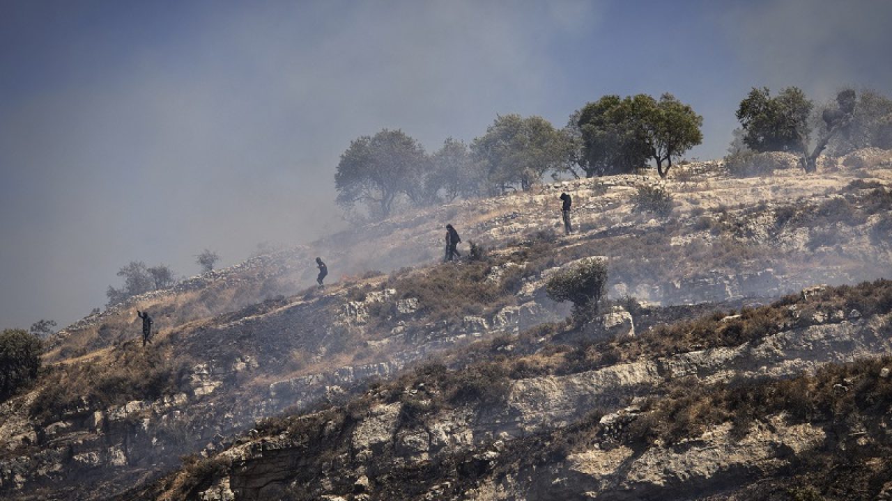 Masked Israeli settlers move down a hill as as Palestinians try to chase them away in the village of Sinjil, in the occupied West Bank on July 4, 2025. Dozens of Israeli settlers and Palestinians clashed on July 4 in the occupied West Bank village of Sinjil, where a march against recent settler attacks on nearby farmland was due to take place. (Photo by JOHN WESSELS / AFP)